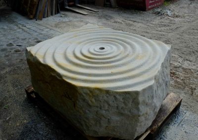 handbehauener Sandstein Brunnen - Quellstein, Wasser sprudelt über wellenförmige Steinfläche
